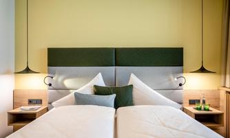 A modern bedroom with two single beds and an elegant headboard design. The walls are light yellow, and there are stylish bedside lamps.