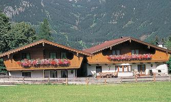 Two traditional chalets with balcony flowers in a picturesque mountain landscape. In the foreground, a green meadow stretches out.