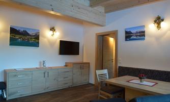 A cozy living room with wooden ceilings and modern furniture. Pictures of mountain landscapes hang on the walls.