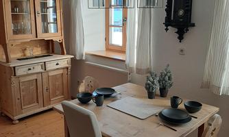 A cozy dining area with a wooden table and chairs. In the background, there is a cupboard and a wall clock.