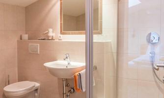A modern bathroom with a shower, a sink, and a toilet. The walls are tiled in light colors and the floor is made of tiles.