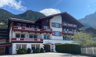 A charming building in the Alps, surrounded by mountains. The clear sky and well-maintained landscape give it an inviting character.