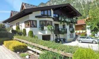 A beautiful two-story house with flower boxes and surrounded by green plants. In the background, you can see mountains and a clear blue sky.