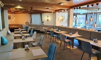 A modern restaurant with bright wooden elements and elegant lighting. The tables are neatly set and the atmosphere is inviting and friendly.