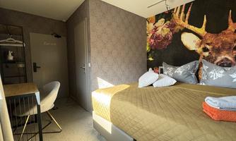 A cozy hotel room with a large bed and decorative pillows. The walls are adorned with a floral pattern, and there is a small desk in the background.