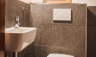 A modern bathroom with gray tiles. There is a sink and a toilet next to a window.