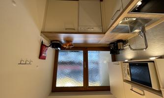 A modern kitchen with bright cabinets and a wooden countertop. It has a window that lets in plenty of light and is well equipped.