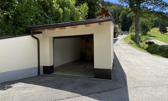 A garage in a quiet place, surrounded by trees and green grass. The sky is clear and sunny.