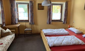 A cozy room with two beds and a sofa. It has large windows and a warm, inviting atmosphere.