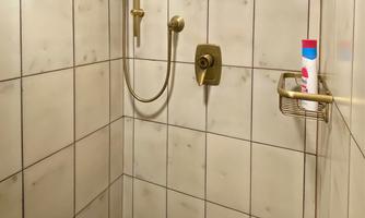A shower cabin with a brown shower floor and tiled walls. A showerhead and a soap dish hang on the wall.