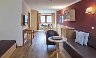 A cozy room with wooden floors, a sofa, and a table. Large windows offer a view of a dining area.