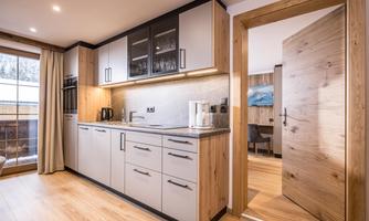 A modern kitchen with wooden and gray cabinets. In the background, an open door is visible, leading to another room.