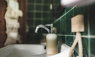 An elegant soap dispenser stands next to a white sink. The walls are tiled with green tiles, creating a calm look.