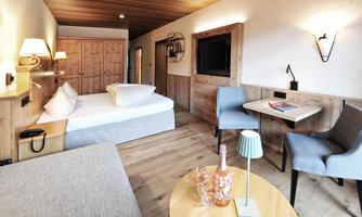 A cozy hotel room with wooden paneling and modern furniture. It includes a double bed, a small table, and a seating area.