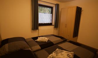 A cozy bedroom with two beds and pillows. A window with curtains and a wardrobe made of light wood are also visible.