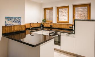A modern kitchen with black countertops and white cabinets. Large windows provide plenty of light and an open atmosphere.
