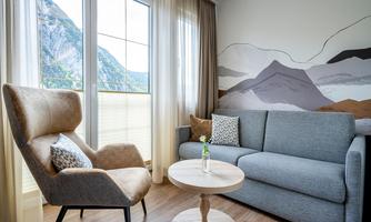 A modern living room with a gray sofa and a cozy armchair. Large windows offer a view of a mountainous landscape.