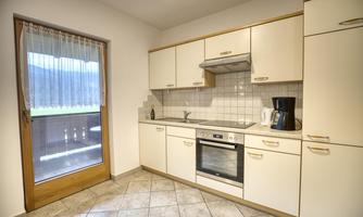 A modern kitchen with white cabinets and a large window. The room is bright and well-equipped with a stove and a coffee machine.