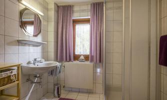 A bright bathroom with a private window. It features a shower, a sink, and elegant curtains.