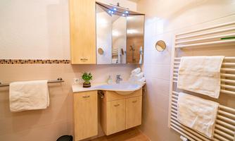 A modern bathroom with wooden cabinets and a large mirror. Towels and a towel warmer are visible, as well as a clean and bright atmosphere.