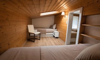 A cozy room with wooden paneling and a skylight. There is a bed, a chair, and a nightstand.