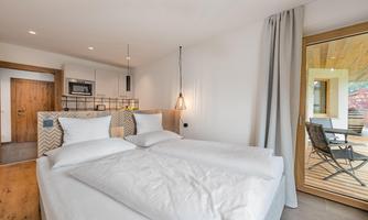 A modern bedroom with a double bed and minimalist furnishings.  
Large windows allow plenty of light in, and the terrace offers a beautiful view.