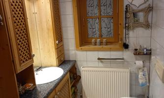 A cozy bathroom with wooden shelves and a sink. Daylight is shining in through a window.