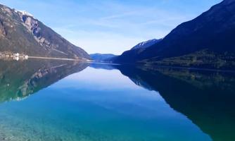 A quiet lake, surrounded by mountains under a clear blue sky. The water perfectly reflects the landscape.