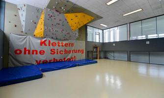 A climbing room with a colorful climbing wall and a large safety notice. The floor is equipped with blue mats.
