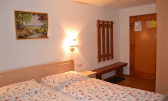 A cozy bedroom with two beds and pretty floral bedding. A painting hangs on the wall, and there is a wooden bench and a wardrobe.