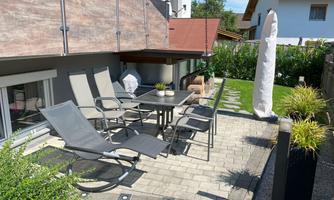 An inviting garden area with a table and several chairs. Surrounded by green vegetation and a cozy atmosphere.