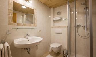 A modern bathroom with a shower, sink, and toilet. The walls are brightly tiled and there is a large mirror.