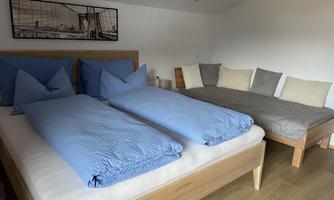A bright bedroom with a double bed and a single bed. The bedding is in shades of blue and gray.