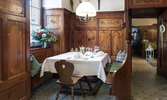 A rustic dining room with wood paneling and a set table. The table is decorated with cloth napkins and glasses, surrounded by cozy seating.