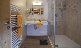 A modern bathroom with a shower and a sink. Towels in orange are decoratively hanging on a towel rack.