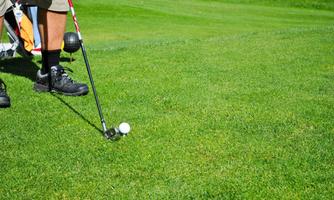 A golfer stands on the grass and prepares for a shot. The golf ball lies in front of him on the green.