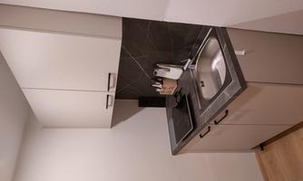A modern kitchen nook with a small stove, sink, and cabinets. The walls are designed in neutral colors, and the floor is made of wood.