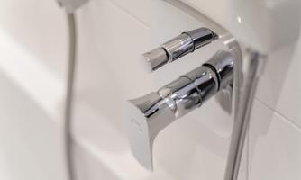 A modern faucet with a shiny chrome finish. It is located on a white wall in the bathroom.
