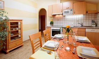 A cozy kitchen with a wooden cupboard and a beautifully set table. On the table are plates, glasses, and a flower in the center.