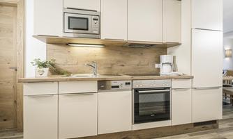 A modern kitchen with bright cabinets, a stove, and a microwave. The floor is wooden and the walls are friendly designed.
