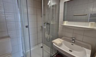 A modern bathroom with a shower, a sink, and a toilet. The walls are tiled and there are towels on the sink.