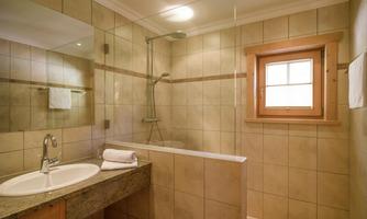 A modern bathroom with a shower and a large mirror. The design is bright and friendly, with tiles and a window.