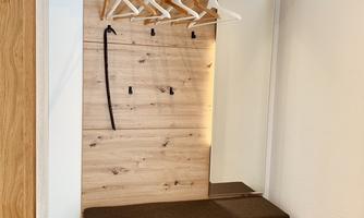 A modern wardrobe area made of wood with a bench and coat hooks. Beneath it are drawers for additional storage space.