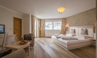 A bright and modern bedroom with a double bed and a cozy armchair. Large windows let in plenty of daylight and create an inviting atmosphere.