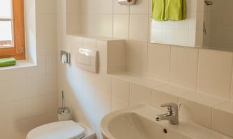 A modern bathroom with white tiles. It includes a sink, a toilet, and green towels.