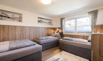 A cozy room with two single beds and a large window. The walls are in warm wooden tones, and there are decorative pictures on the wall.