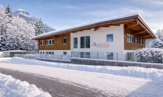 A modern building in chalet style, surrounded by snow-covered trees. The sky is clear and the landscape appears wintry and calm.
