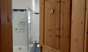 A bathroom with a wooden ceiling and a large window. Visible are a bathtub, a shower, and bright tiles.