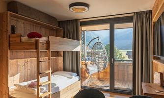 A cozy room with a loft bed and a single bed. Large windows offer a view of the balcony and the surrounding nature.