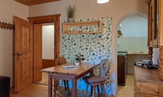 A cozy dining corner with a wooden table and two chairs. The walls are decorated with a blooming pattern, and the door leads to another room.